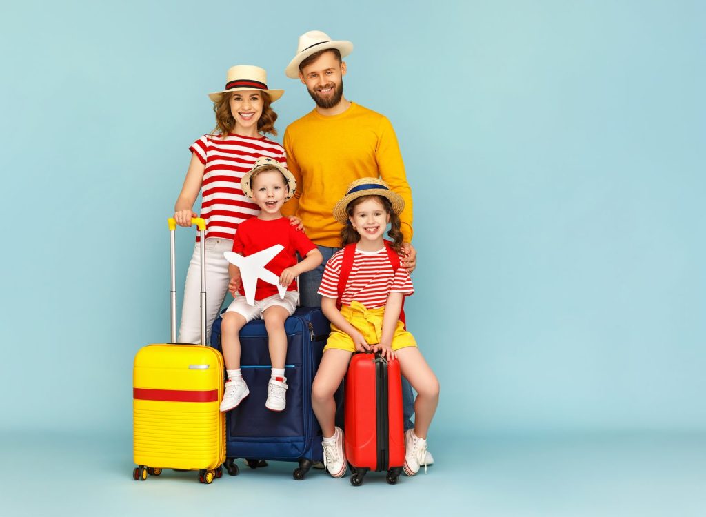 Family of four with colorful suitcases posing for a travel photo against a blue background.